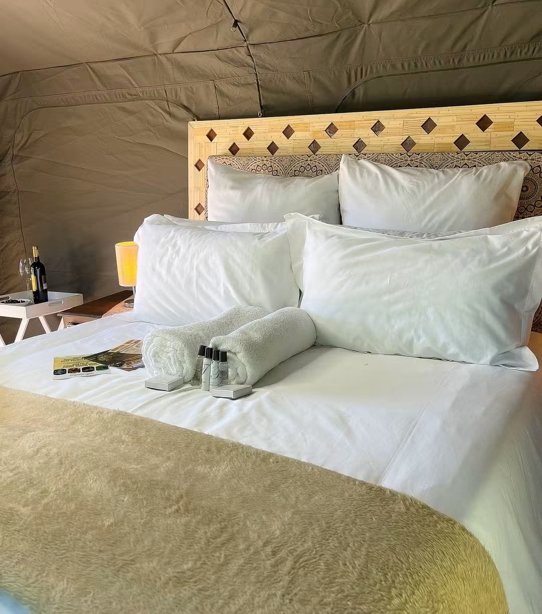 A glamping bed with pillows, white bedding and folded towels inside a canvas tent